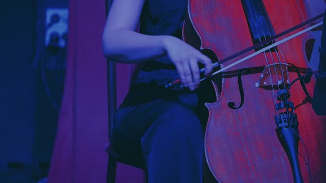 Close-up of a female musician playing the cello in spectacular blue lighting. The musician moves the bow gracefully over the strings of the instrument. Classical music