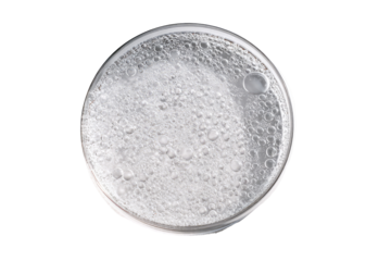 Circular petri dish filled with foamy, light gray liquid.  Small bubbles and liquid droplets are visible