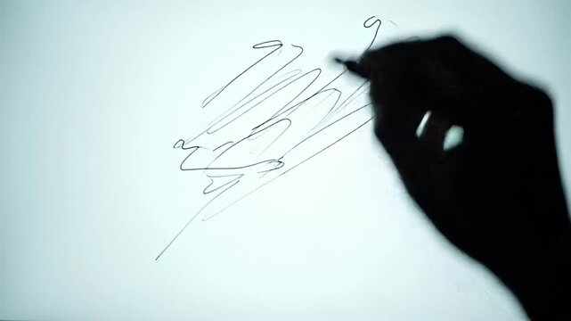 Silhouette of a hand sketching scribbles on a white surface with a marker