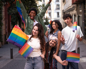 Fototapeta premium Group of cheerful young activists holding rainbow flags celebrating gay pride in city street
