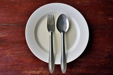 Spoon and fork on empty plate placed on brown wooden table, Top view