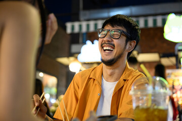 Asian man laughing while having dinner with a friend at night market