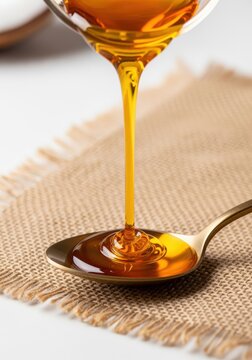 Golden honey pouring from a glass into a spoon, closeup shot, isolated on white background