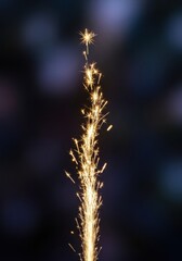 Obraz premium Sparkler Firework with Bright Golden Sparks Against Dark Background