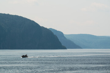 Boat creating ripples in water with distant hills under soft blue sky.
