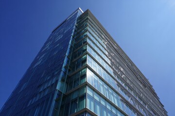 Low angle view of a modern glass skyscraper against a clear blue sky on a sunny day