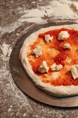 Pizza dough with sauce and cheese, uncooked, on a table.