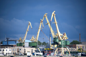Fototapeta premium Industrial Port with Large Yellow Cranes on a Bright Cloudy Day