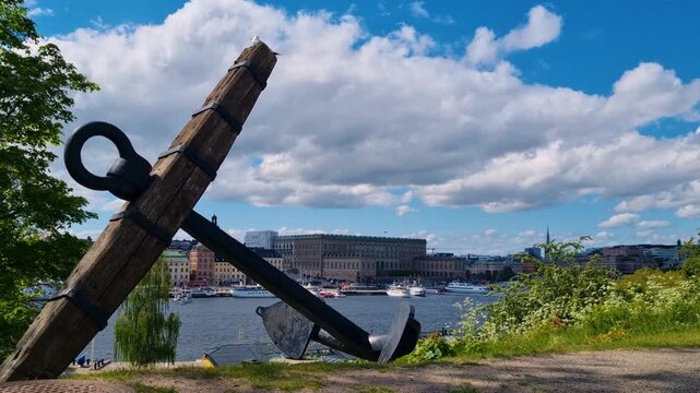 View of a weathered anchor atop a hill, overlooking Gamla Stan and Str&ouml;mmen Bay under a partly cloudy spring sky in Stockholm, Sweden
