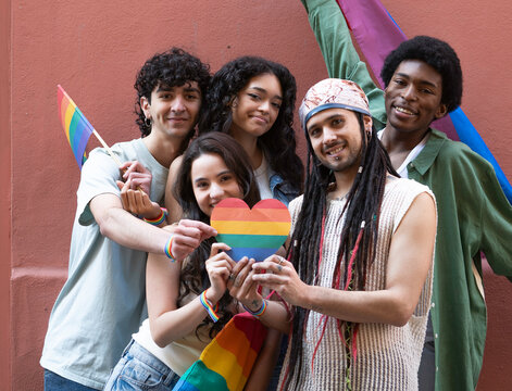 Group of young activists holding rainbow heart and flags, celebrating diversity, inclusivity, and lgbtq rights during pride month