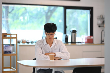Thoughtful male employee sitting alone at a table with a paper coffee cup