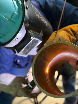 Industrial welder welding metal pipe with GTAW TIG torch, protective gloves, helmet, safety equipment, factory workshop, precision welding process, fabrication, repair, craftsmanship, heavy industry 