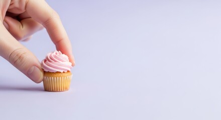 Hand picking up a tiny pink cupcake with delicate frosting