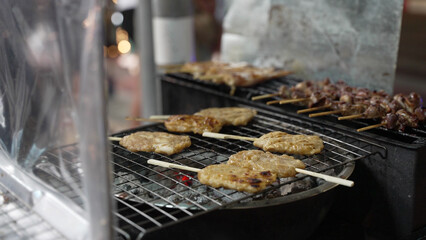Close up of cooking grilled pork skewer, authentic Thai Moo Ping street food. Night market on Yaowarat road, Chinatown, Bangkok
