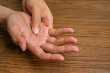 Close-up of hand pain from repetitive work strain; one hand presses the palm of the other over a wooden desk, highlighting ergonomic stress and musculoskeletal discomfort.