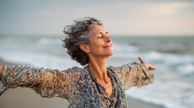 happy mature woman with arms outstretched feeling the breeze at beach beautiful middle aged woman with arms up dancing on beach mid lady feeling good and enjoying freedom at sea copy space no logos n