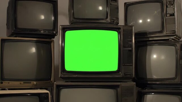 Stack of Vintage Tube TVs with Green Screen - A pile of old, dusty tube televisions is stacked against a gray background.