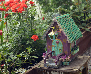 Cute fairy doll house and roses on the flowerbed in the greenhouse. Lovely miniature for greeting cards, wedding or birthday concept, real estate, downsizing, home ownership. Vintage background