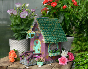 Cute fairy doll house with flowers on the table in the greenhouse. Lovely miniature for greeting cards, wedding or birthday concept, real estate, downsizing, home ownership. Vintage background