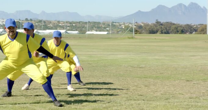 Diverse male athletes initiating side shuffle on grassy field, warming up in yellow jerseys