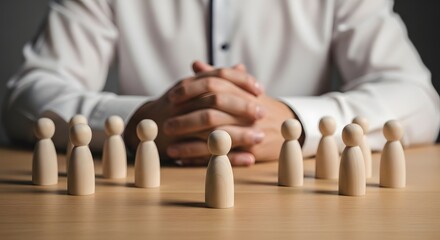 Wooden figures stand before a person with clasped hands on a table in a business setting