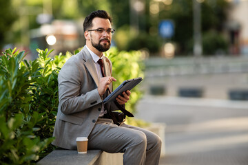 Obraz premium Businessman using digital tablet while sitting outdoors with coffee