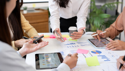 cropped shot of a team of diverse professionals collaborating around a table. They are using a laptop and a tablet with charts and graphs, pointing at the screens and discussing a project.