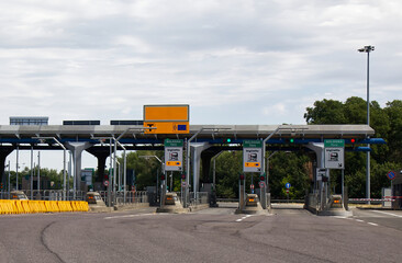 A view of a modern highway toll booth plaza with multiple lanes under a cloudy sky, showing ticket and electronic payment options near Bologna, Italy.