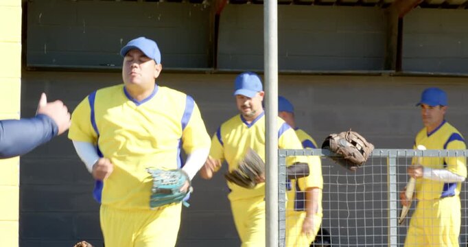 Male baseball team at dugout responding to coach signal by grabbing gloves and jogging, huddling