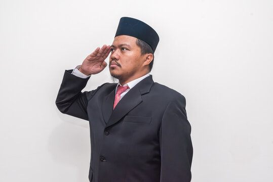 Patriotic Asian man in a traditional peci cap and formal suit giving a solemn salute. - Powered by Adobe
