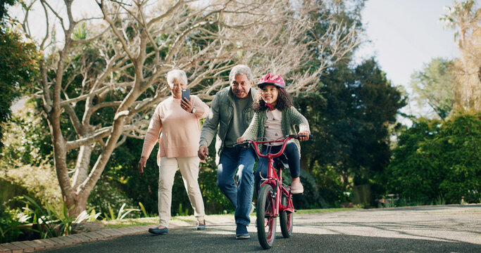 Grandparents, child and learning with bike for picture or memory of family bonding outdoor. Grandmother, grandfather and girl ride bicycle, teaching cycling and phone for photo with happy generations