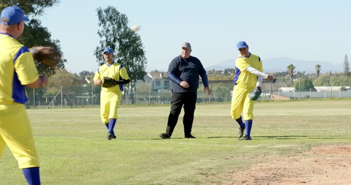 Clapping umpire prompting male teammates cycling ball throws on infield, warming up for game