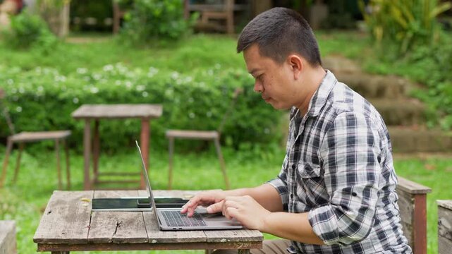  Young businessman sitting at a table in an outdoor cafe or coworking space and using a laptop computer.