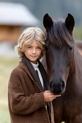 Fototapeta premium Blond caucasian child with brown horse outdoors