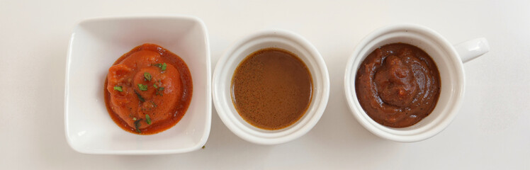 Three small white bowls filled with different types of sauces on white background, top view