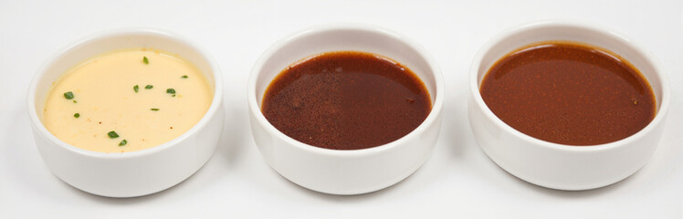 Three white bowls filled with creamy, spicy, and tangy sauces on white background