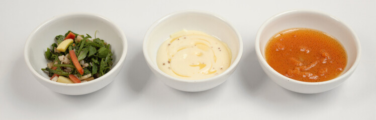 Three white bowls with salad, creamy sauce, and vinaigrette on white background