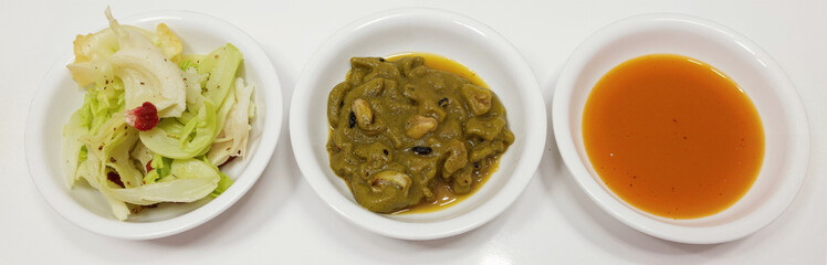 Cabbage salad, green curry with mushroom, and orange soup in white bowls on white background