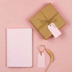 Flat lay of a gift box with tags, a notebook, and a wheat stalk on a pink colored background