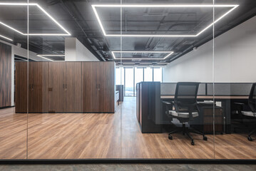 Open office space featuring wooden accents and modern furniture. Glass wall view of clean, modern office with organized workstations