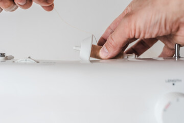 Dressmaker preparing working place and sewing machine for tailoring at home. Thread spool placed on sewing machine by male hands, close-up setup process