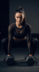 Fototapeta premium Woman in black mesh workout outfit performing plank with push-up blocks on dark background. Bodyweight training and functional fitness for equipment promotions and personal coaching services