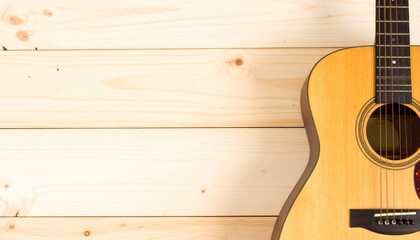 Fototapeta premium Acoustic guitar positioned on the bottom-right corner over a wooden floor background. Warm tungsten lighting creates an inviting and creative music scene with copy space.