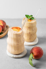 Two glasses of smoothie with peach and banana in a glass on a light background with tropical fruits.