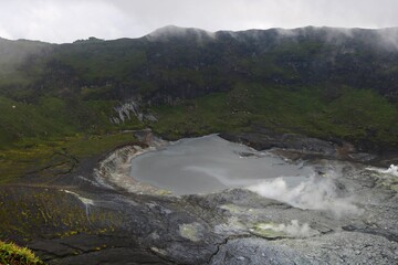 Aerial view of an active volcanic crater emitting white smoke with rugged rocky terrain