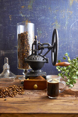 Glass cup of freshly brewed black coffee on a rustic wooden table with ground coffee, beans, and a vintage grinder in the background, styled in cozy farmhouse and artisan coffee photography