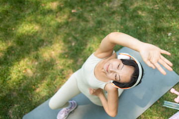 Young Asian woman in sportswear stretching body on fitness mat at public park, doing yoga. Healthy lifestyle, sport. Fitness. Woman doing yoga in morning park.