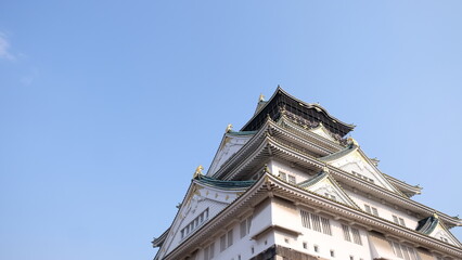Fototapeta premium Osaka Castle in Japan against clear blue sky, showcasing traditional Japanese architecture and ornate roof details.
