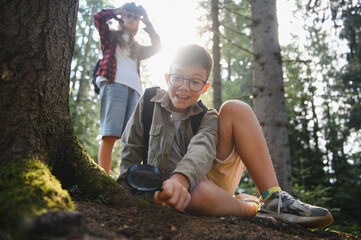Young explorers investigating nature with magnifying glass in forest