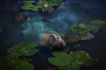 girl floats gracefully in a tranquil pond, partially submerged and surrounded by large lily pads....